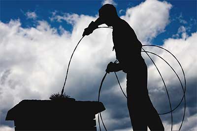 chimney service in Red Bank, chimney sweep on roof top backlit with a brush in the top of the chimney