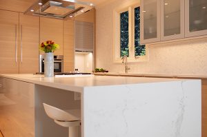 Custom home builder in Summit, modern kitchen shown in tan and white with vase of flowers on countertop